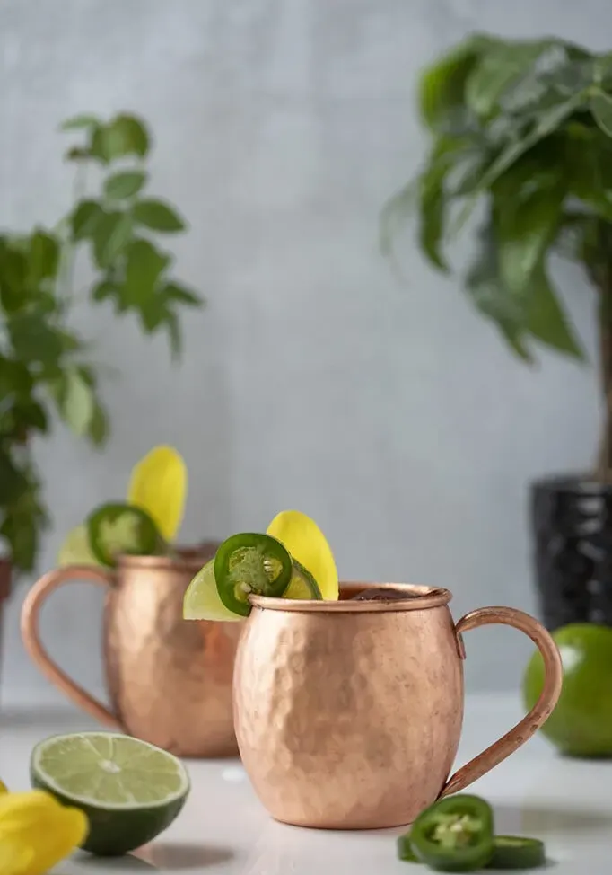 dva medené hrnčeky mulice vedľa limetiek a plátkov jalapeňo.' title=