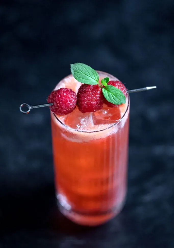 Blick von oben auf einen großen roten Cocktail, garniert mit Himbeeren und Minzblättern' title=