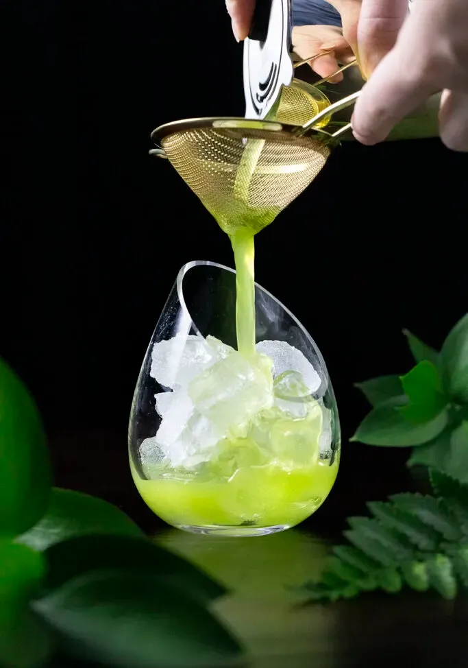 verser une boisson verte à travers une passoire à mailles fines.' loading='lazy' title=