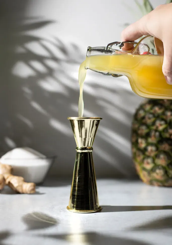 despejando xarope de abacaxi e gengibre em uma coqueteleira.' title=