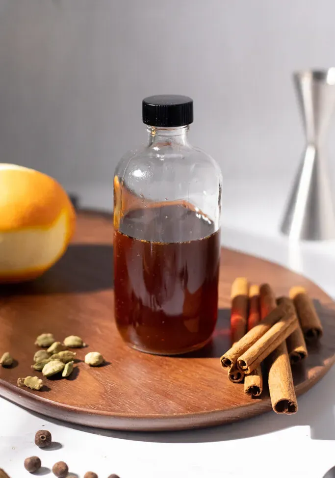 ciemnobrązowy syrop w butelce z przyprawami i pomarańczą.' title=