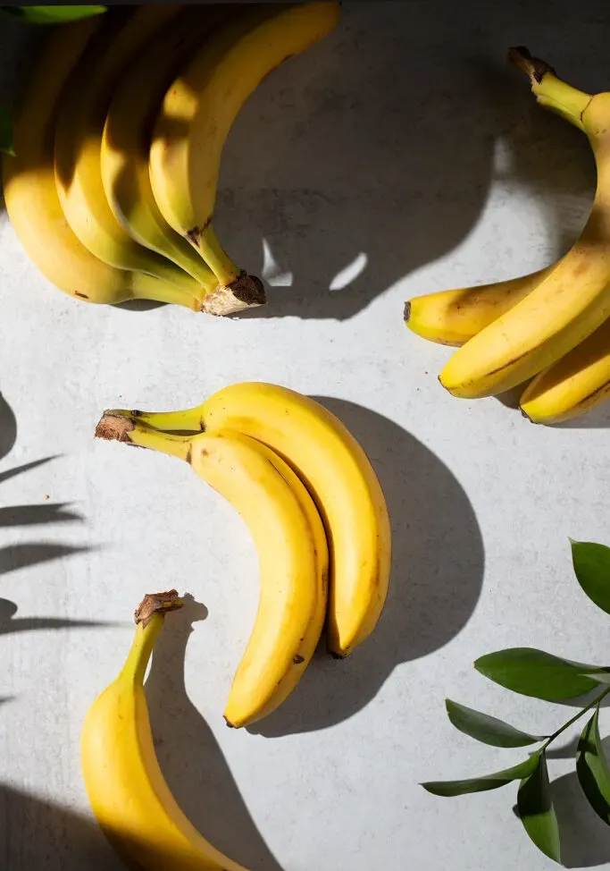 diverse banane su un tavolo grigio con foglie verdi.' loading='lazy' title=