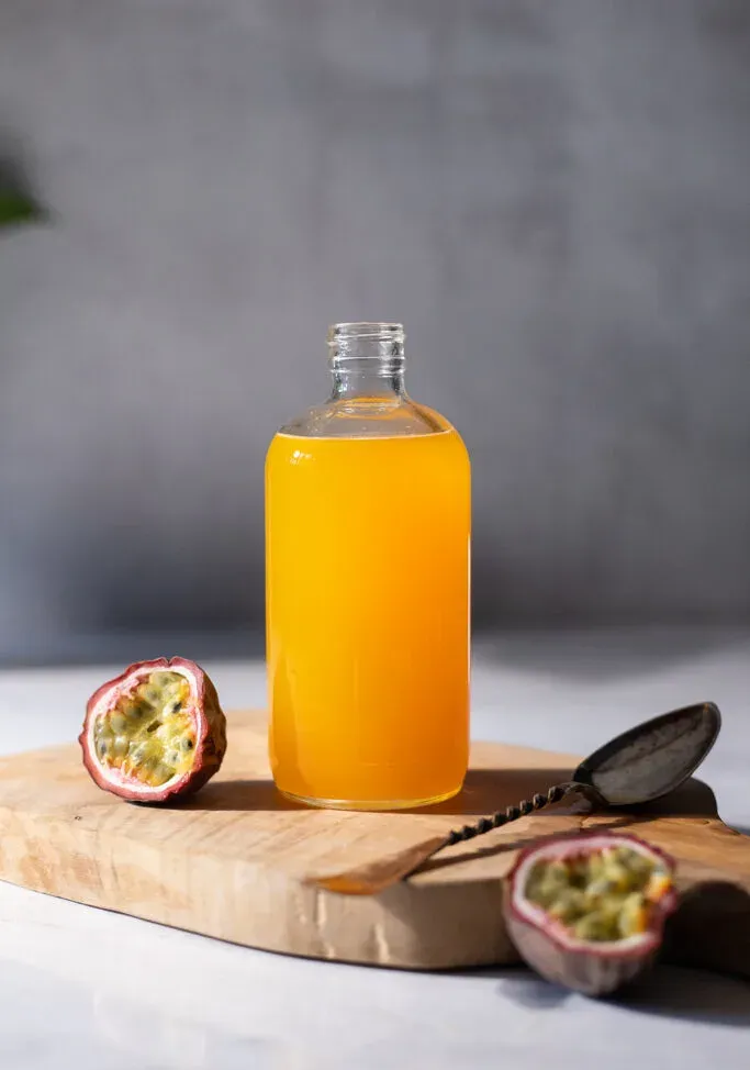 בקבוק זכוכית פתוח מלא בסירופ צהוב על קרש חיתוך מעץ.' loading='lazy' title=