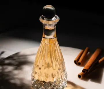 liquido giallo pallido in una bottiglia di vetro acidato vintage accanto a bastoncini di cannella.' title=