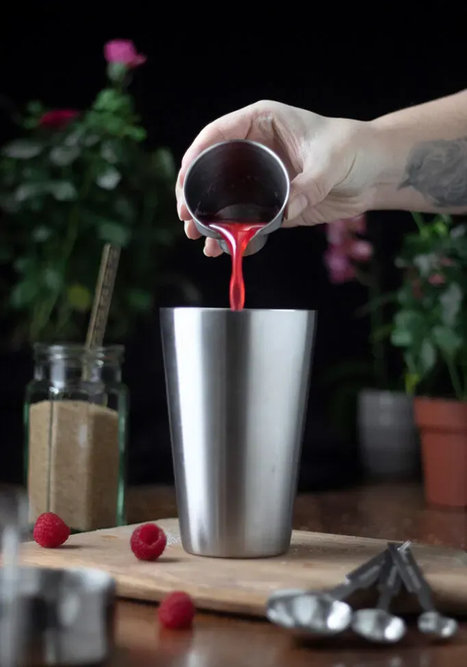derramando xarope vermelho brilhante em uma coqueteleira.' loading='lazy' title=