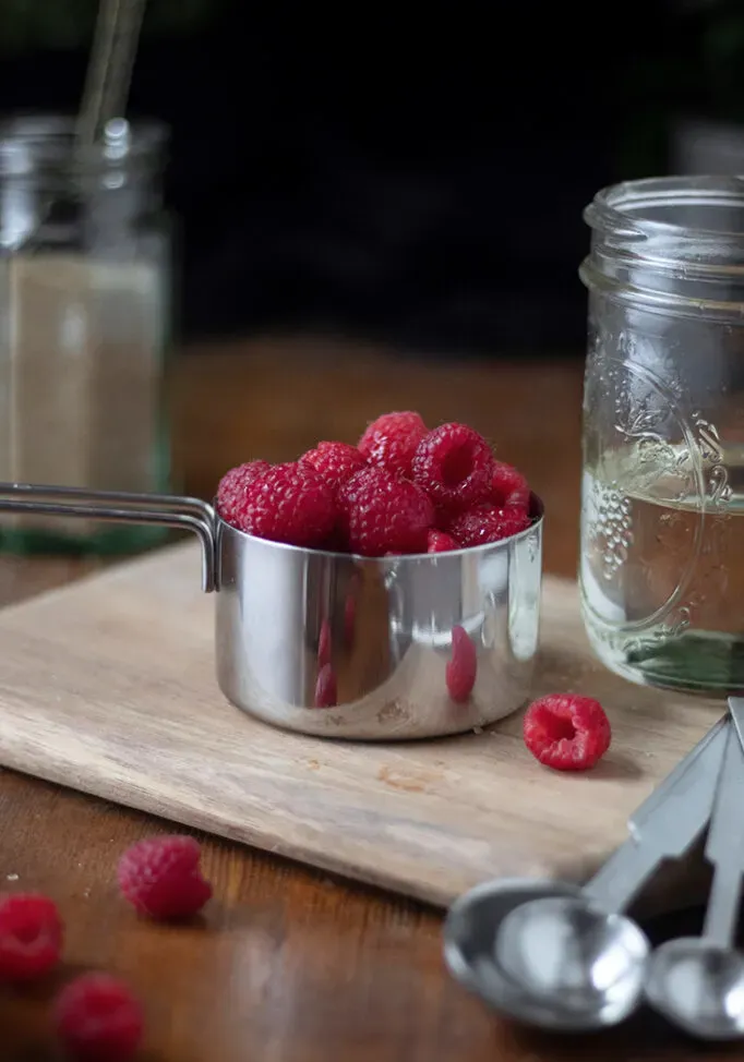 um copo medidor de metal cheio de framboesas.' loading='lazy' title=