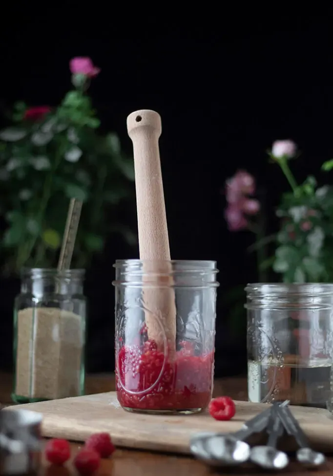 um misturador de madeira em um pote cheio de purê de framboesas.' title=