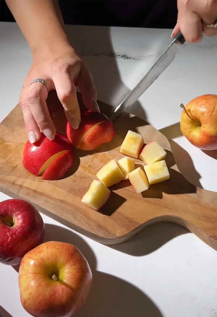 나무 커팅 보드에 빨간 사과를 자르는 손.' loading='lazy' title=