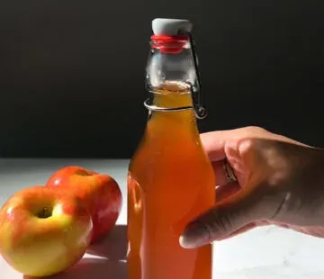 황금빛 갈색 시럽으로 채워진 유리 스윙 탑 병을 손에 들고 있습니다.' title=