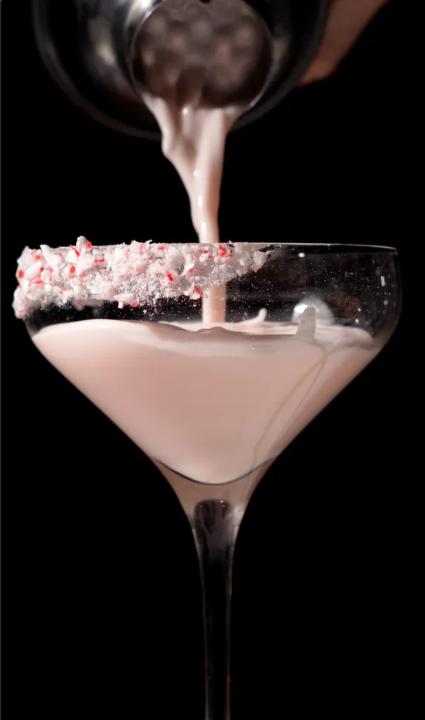 Gießen Sie eine blassrosa, cremige Flüssigkeit in ein Cocktailglas mit zerkleinerten Zuckerstangenstücken.' title=