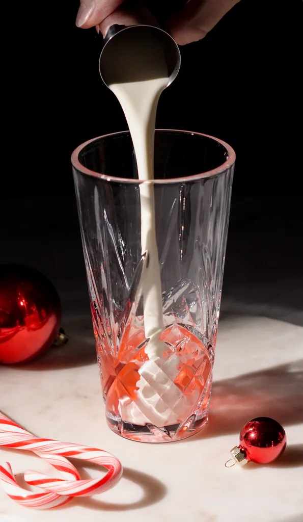 Sahne aus einem Metallbecher in einen Cocktailshaker aus Glas gießen.' title=