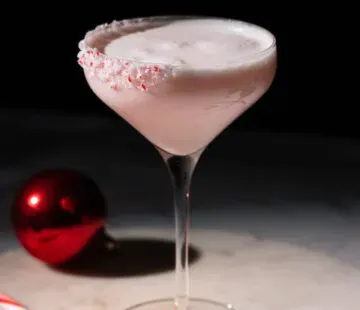 Cocktailglas gefüllt mit rosa cremigem Getränk neben Zuckerstangen.' title=