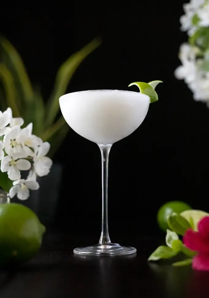zmrzlý bílý koktejl v dlouhém kupé sklenice na černém pozadí s limetkami' loading='lazy' title=