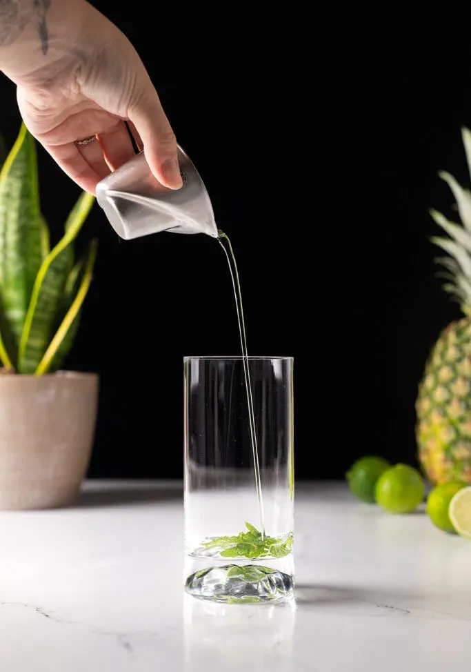 민트 잎이 달린 키가 큰 유리잔에 간단한 시럽을 붓습니다.' loading='lazy' title=