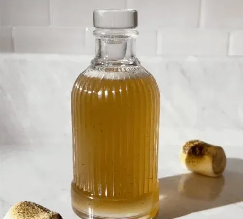 bottiglia di vetro di sciroppo d'oro accanto a due marshmallow tostati.' title=