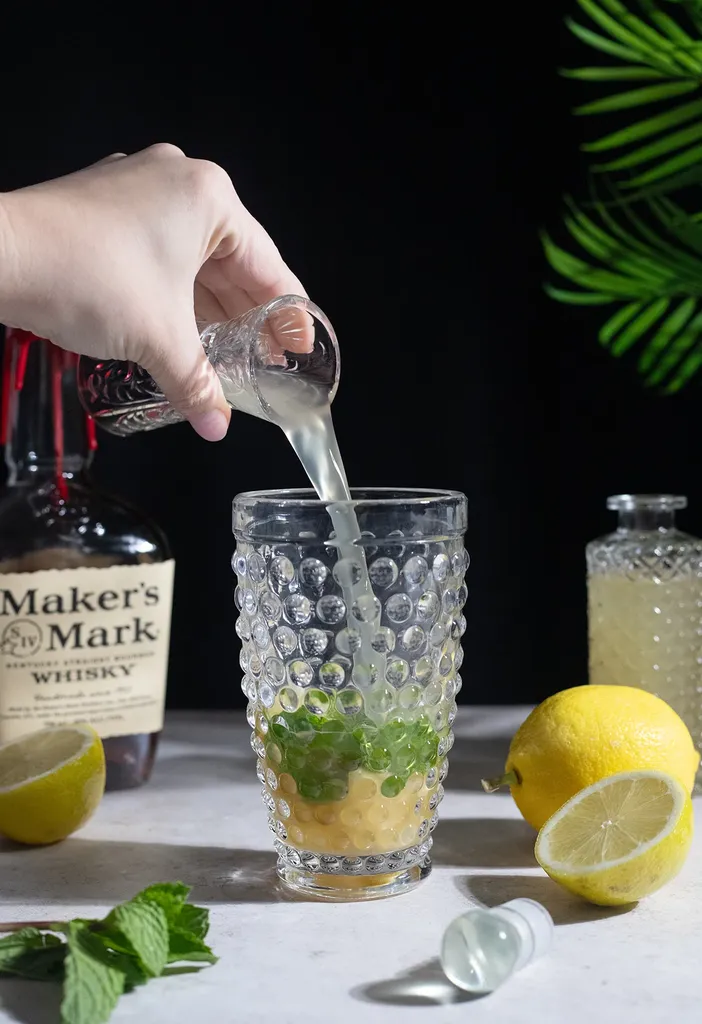 Verter jugo de limón del jigger de vidrio en una coctelera de vidrio.' loading='lazy' title=