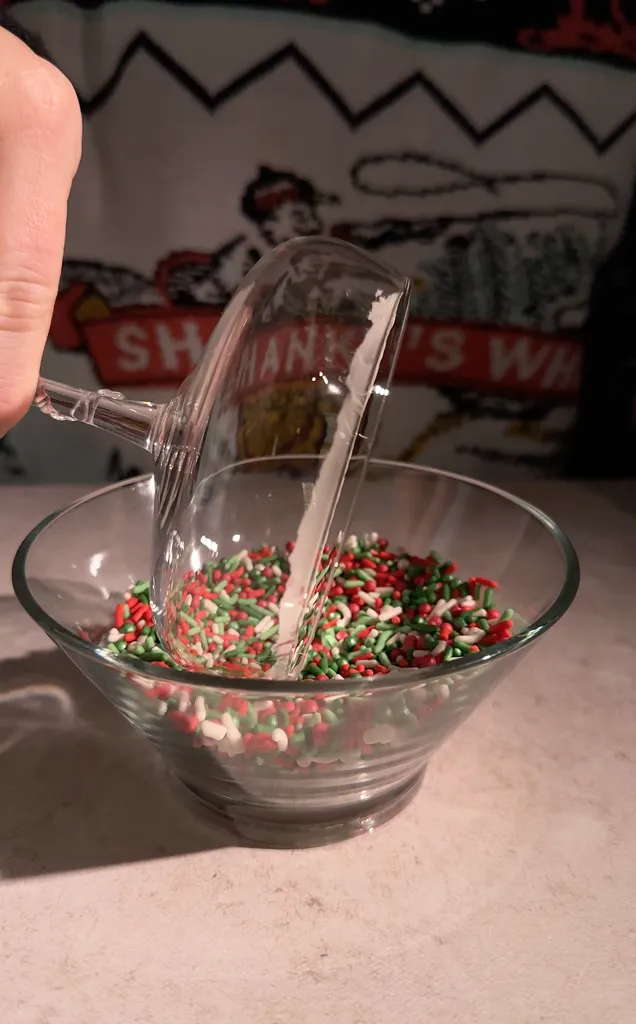 koktailový pohár ponorený do misky s červeným a zeleným posypom.' title=