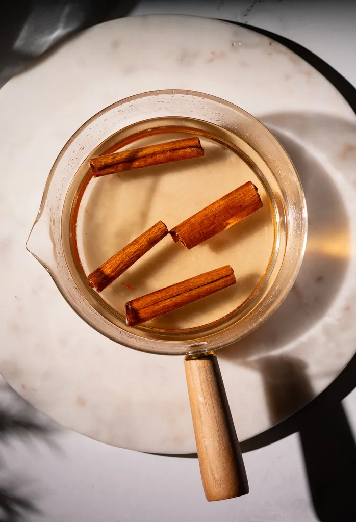 liquido giallo pallido e quattro bastoncini di cannella in un pentolino di vetro.' title=