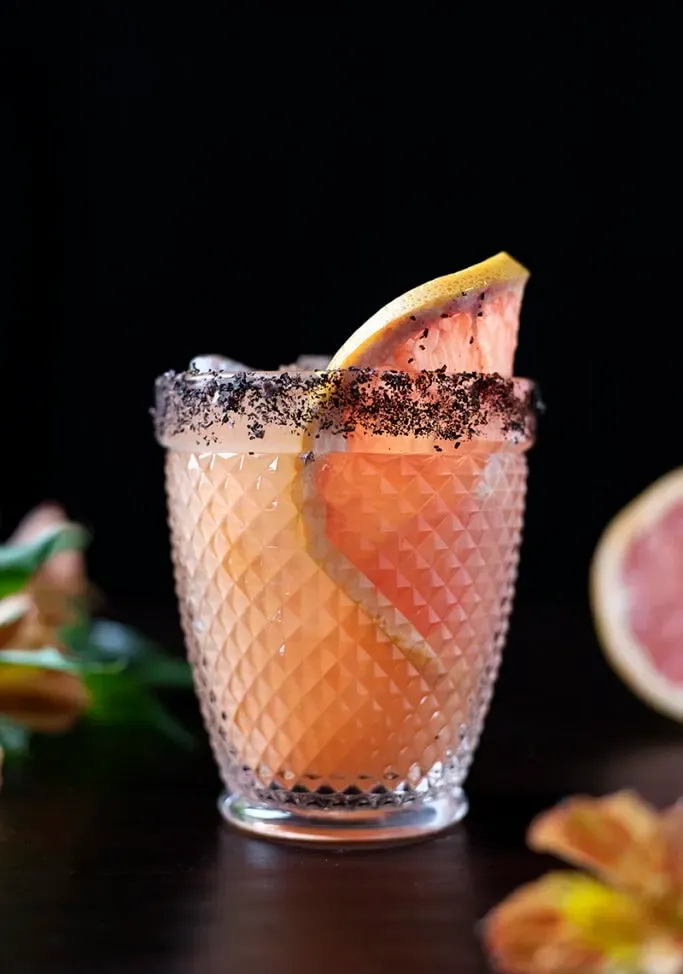 um copo de gelo cheio de suco de toranja e decorado com uma roda de toranja.' title=