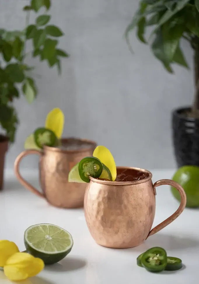 coquetéis de mula de Moscou em canecas de cobre com fatias de jalapeño.' title=
