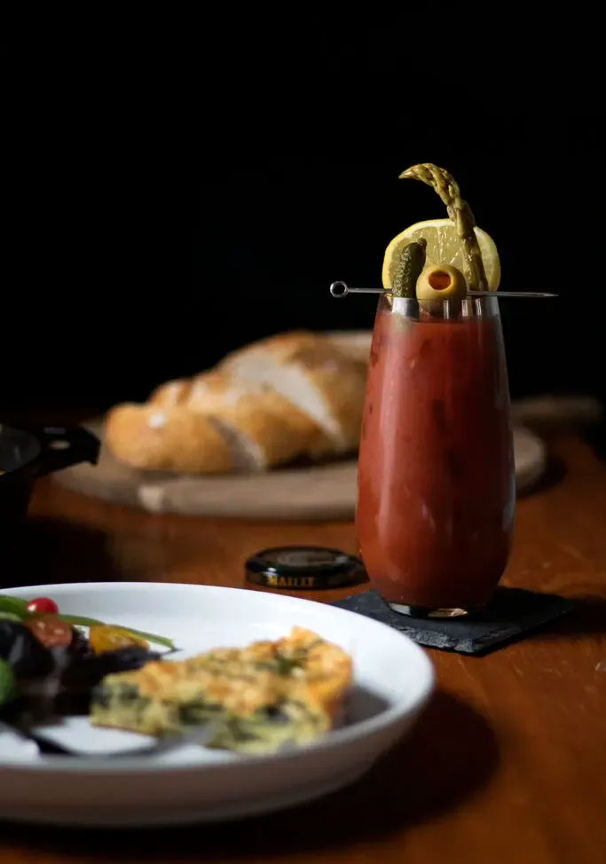 um coquetel Bloody Mary ao lado de uma fritada de ovo e pão fatiado.' title=