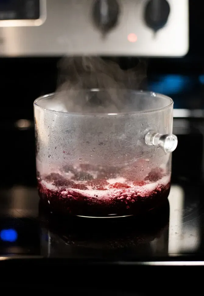 끓는 블랙베리 시럽을 넣은 유리 냄비에서 증기가 솟아오르고 있습니다.' loading='lazy' title=