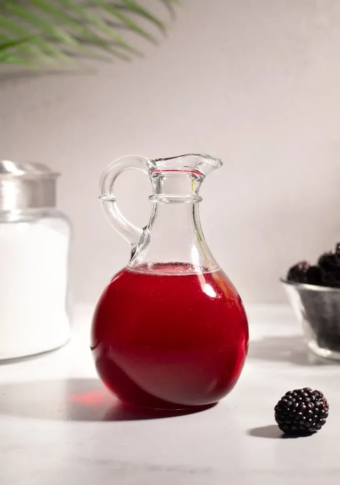 흰색 테이블에 진한 빨간색 블랙베리 시럽 투수.' title=