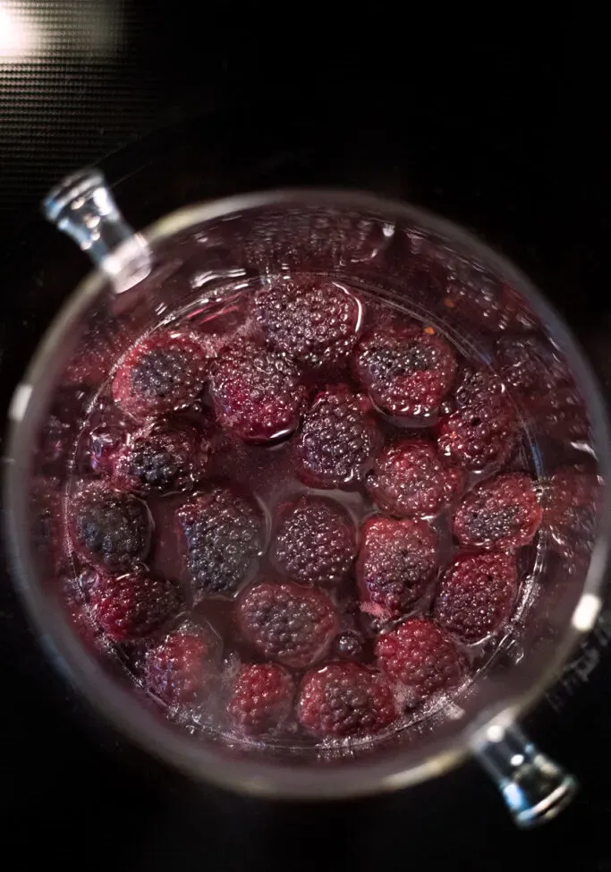 쿡탑 위의 유리 냄비에 액체에 담긴 붉은색 요리 블랙베리.' title=