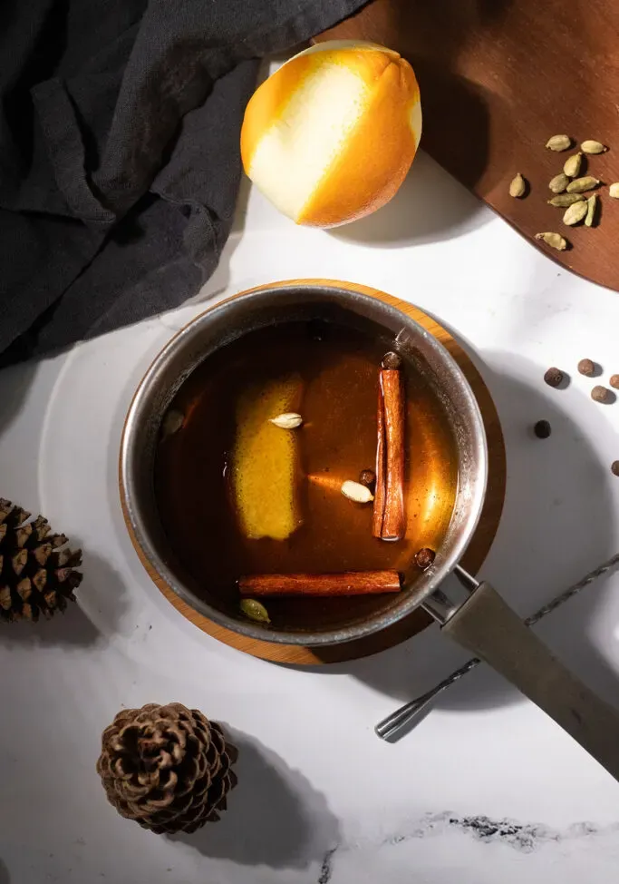 냄비에 향신료와 오렌지 껍질을 넣은 갈색 액체.' title=