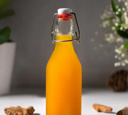 zblízka fľaše kurkumového sirupu vedľa kúskov koreňa kurkumy.' title=