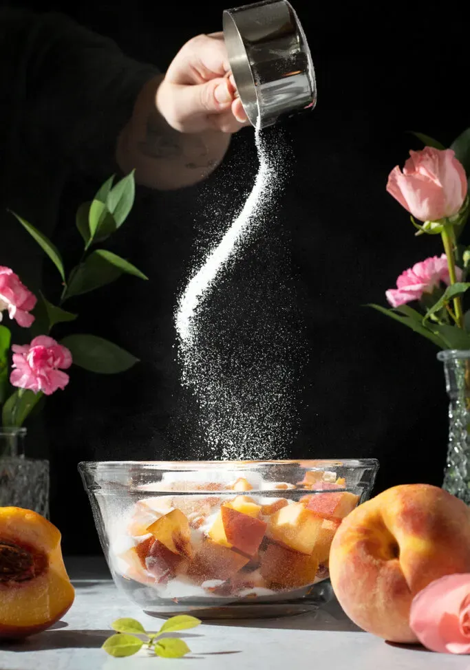 מפזרים סוכר על אפרסקים בקערה.' title=