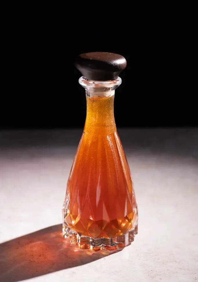 piccola bottiglia di vetro acidato con tappo marrone riempita con sciroppo marrone chiaro.' title=