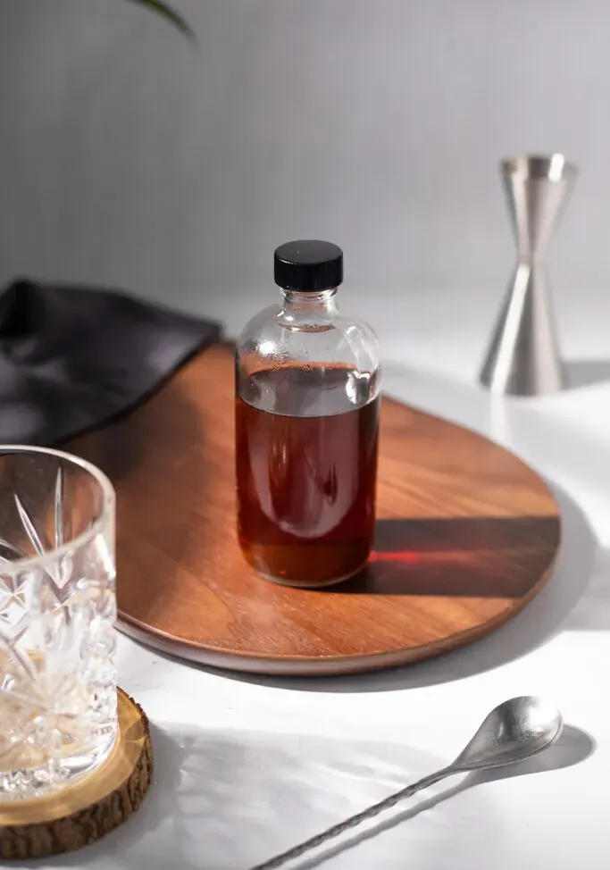 okrągła butelka bostońskiego brązowego syropu demerara na desce do krojenia.' title=