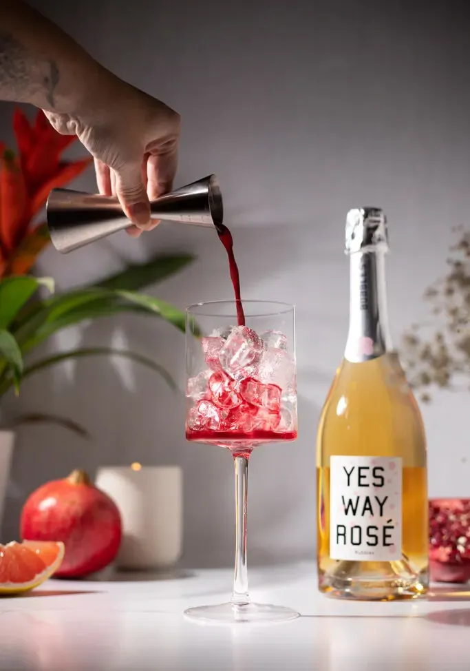 Verser du jus de grenade rouge foncé dans un verre à vin rempli de glace.' loading='lazy' title=