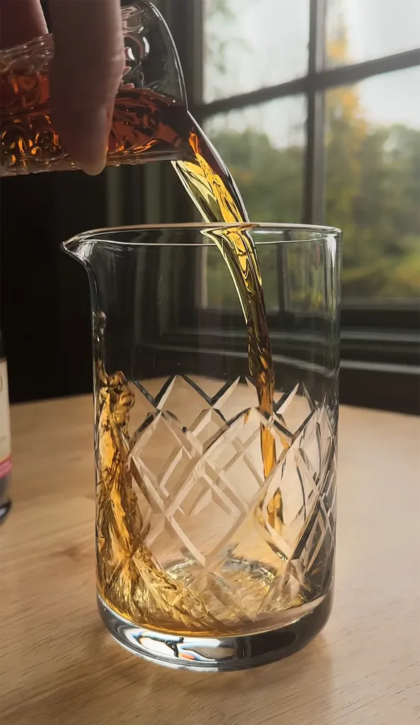 מזיגת משקה חריף חום מג'יגר לכוס ערבוב.' loading='lazy' title=