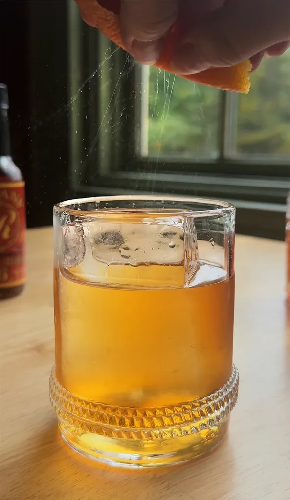 שמנים שמתזים מקליפת תפוז מעל קוקטייל בכוס לואובול.' title=