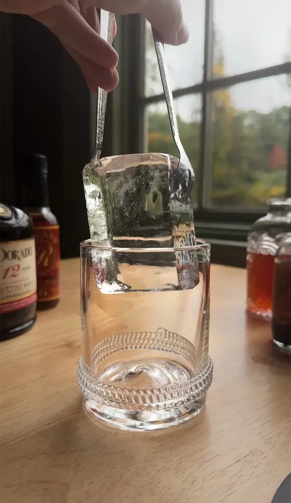 커다란 투명한 얼음 조각을 유리잔에 넣는 금속 집게.' title=