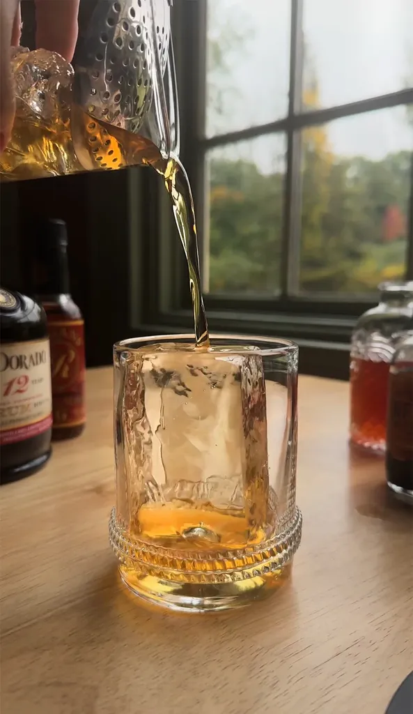 믹싱 글라스의 황금색 액체를 로우볼 글라스에 붓는 모습.' title=