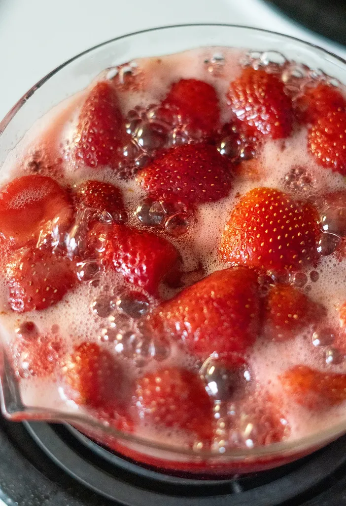 primo piano di fragole allo sciroppo bollente in una padella di vetro.' title=