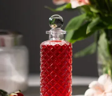 bottiglia di vetro acidato di sciroppo rosso accanto a fragole e fiori bianchi.' title=