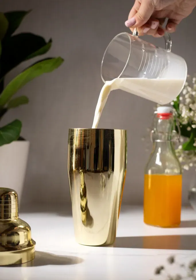 יוצקים חלב לתוך שייקר קוקטייל מוזהב.' title=