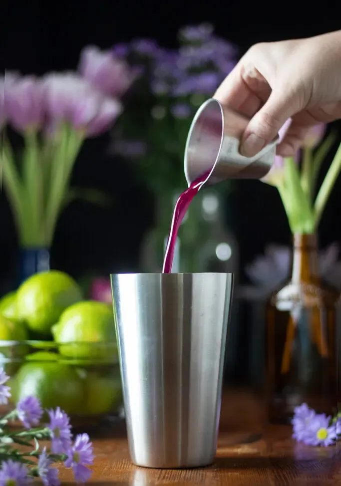 versare lo sciroppo rosa da un jigger in uno shaker.' title=