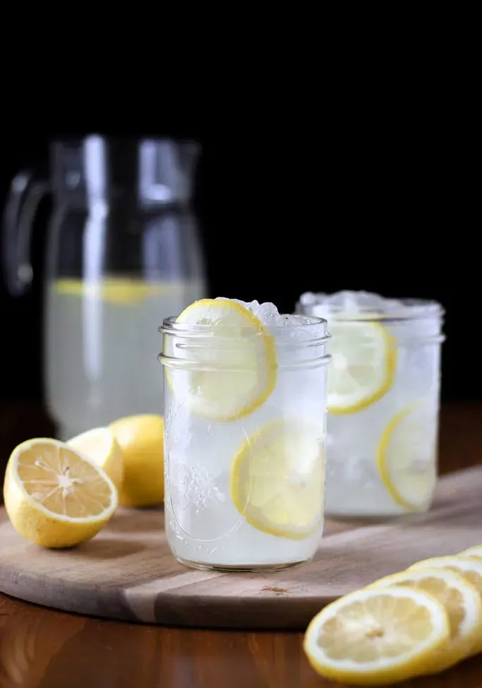 שתי כוסות לימונדה עם פרוסות לימון וקנקן.' title=