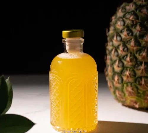 sciroppo giallo in una bottiglia di vetro accanto a un ananas.' title=