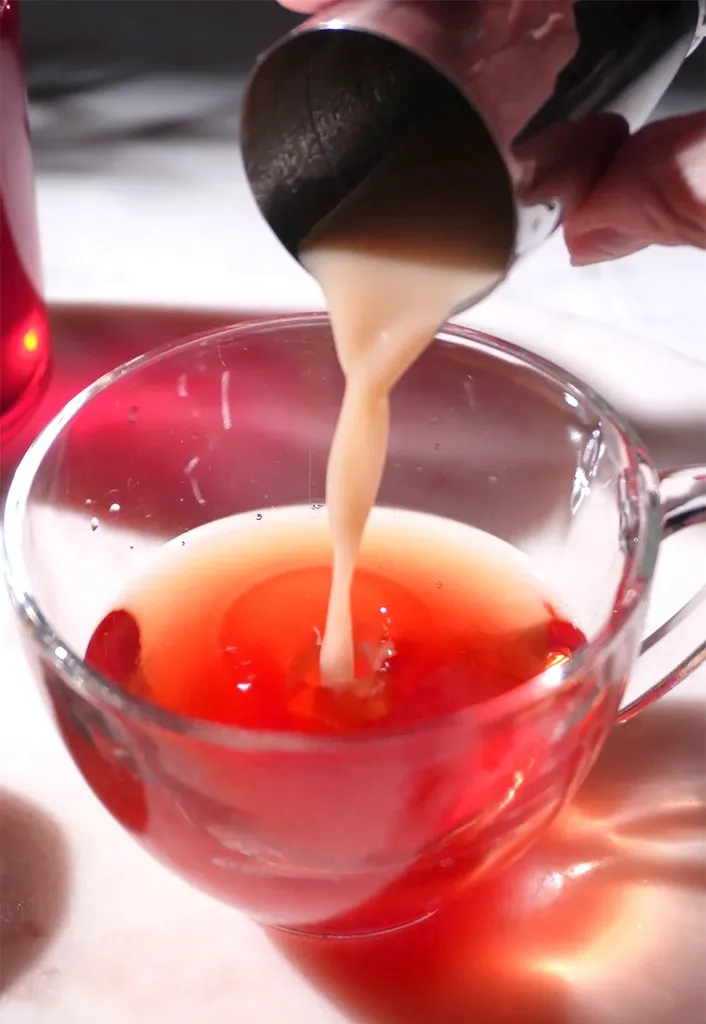 derramando suco de gengibre leitoso de uma coqueteleira de metal em uma xícara de chá de vidro.' title=