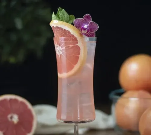 pohár na hurikán naplnený ružovým kokteilom a ozdobený orchideou.' title=