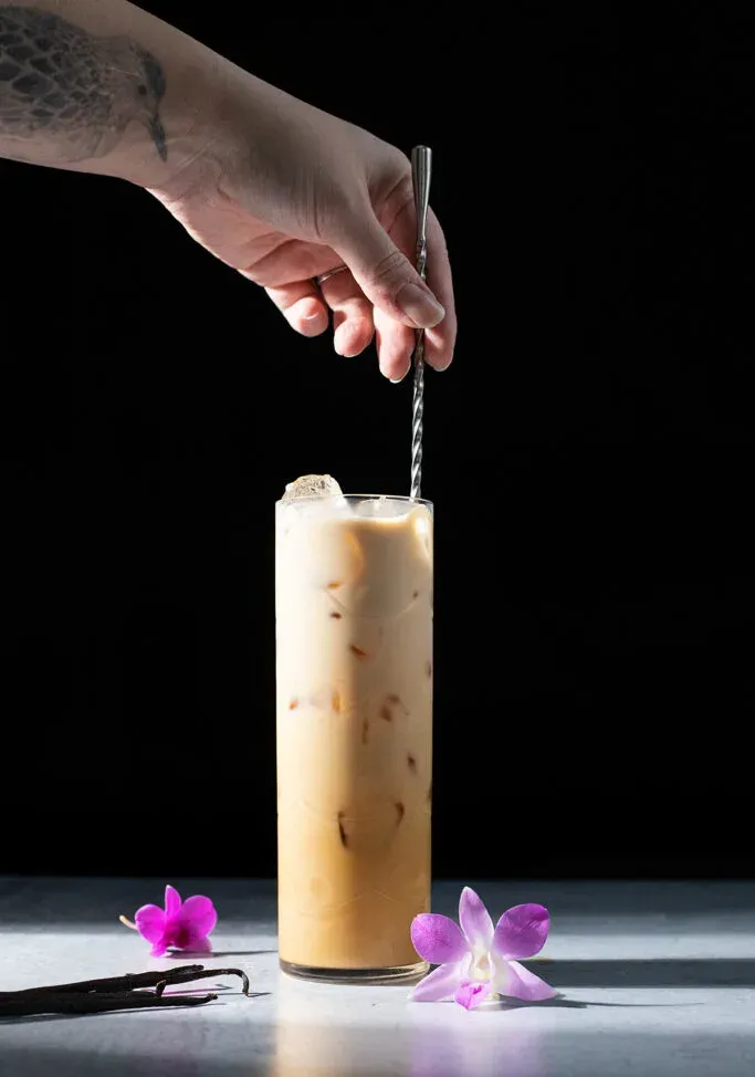 mescolando un caffè freddo con un lungo cucchiaio.' title=