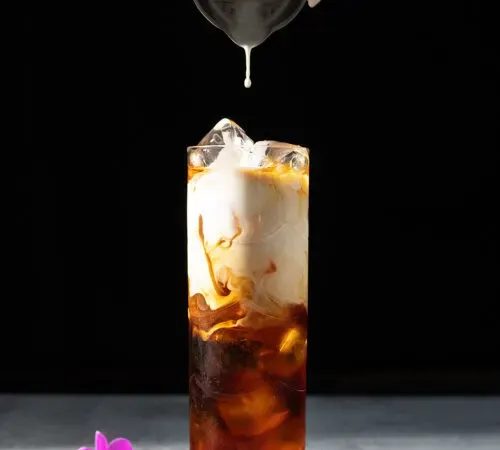 una goccia di panna che cade nel caffè freddo.' title=