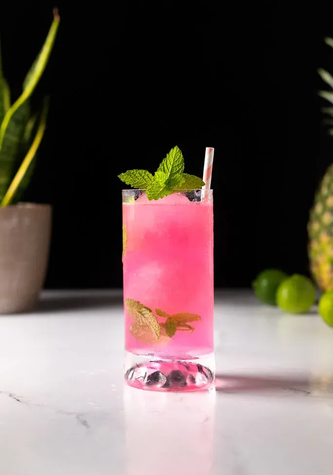 ミントの葉と紙ストローが付いたピンクのハイボールドリンク。' title=