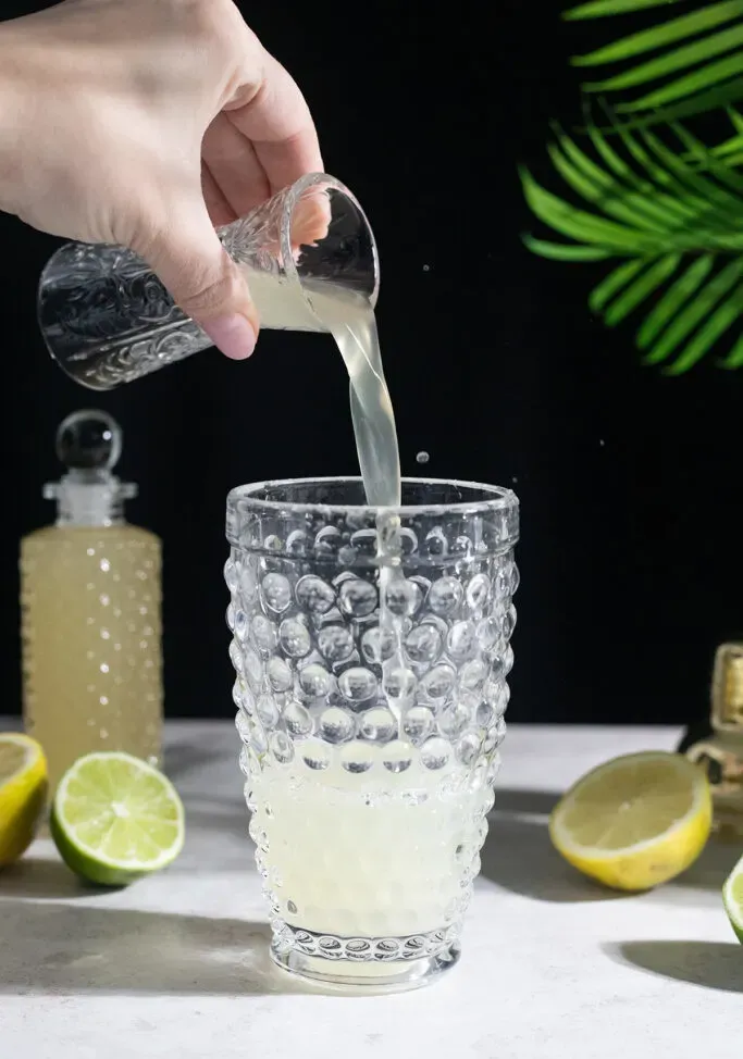 מוזגים סירופ ג'ינג'ר לתוך שייקר קוקטיילים מזכוכית.' title=